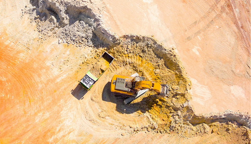 Browne Group - Aerial view of an excavator loading dirt into a dump truck at a construction site.