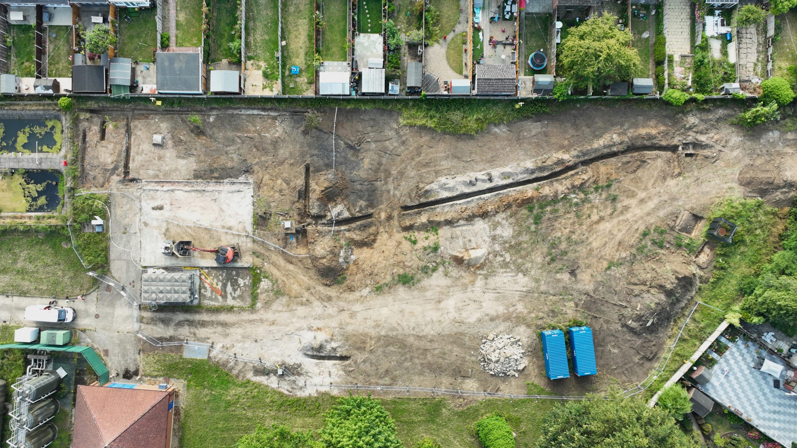 Browne Group - Aerial view of a construction site with machinery, dirt paths, blue containers, and nearby buildings.