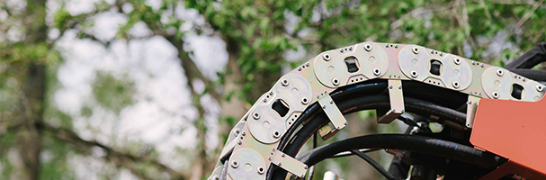 Browne Group - Close-up of a metal cable carrier with black cables, set outdoors with blurred trees in the background.