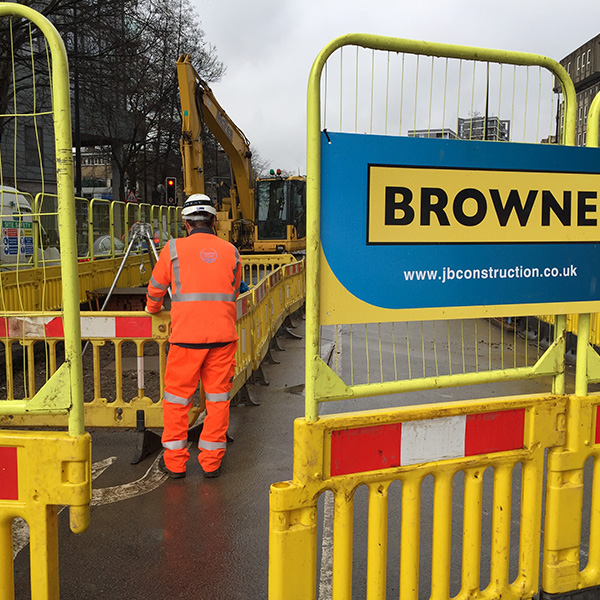 Browne Group - A construction worker in orange gear stands near yellow barriers at a city roadwork site.