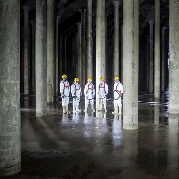 Browne Group - Five workers in white protective suits and yellow helmets stand in a large, empty concrete columned space.