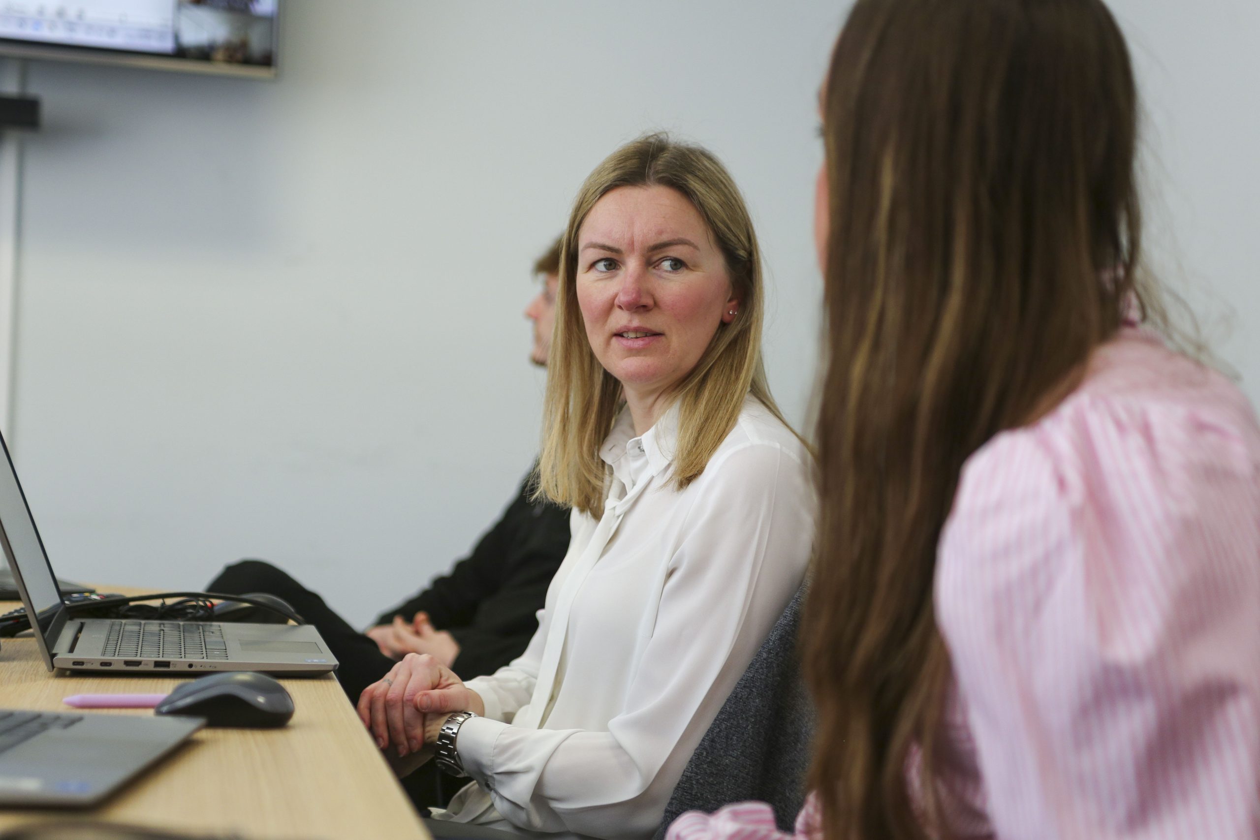 Browne Group - Three women sit at a desk with laptops, engaged in conversation in an office setting.