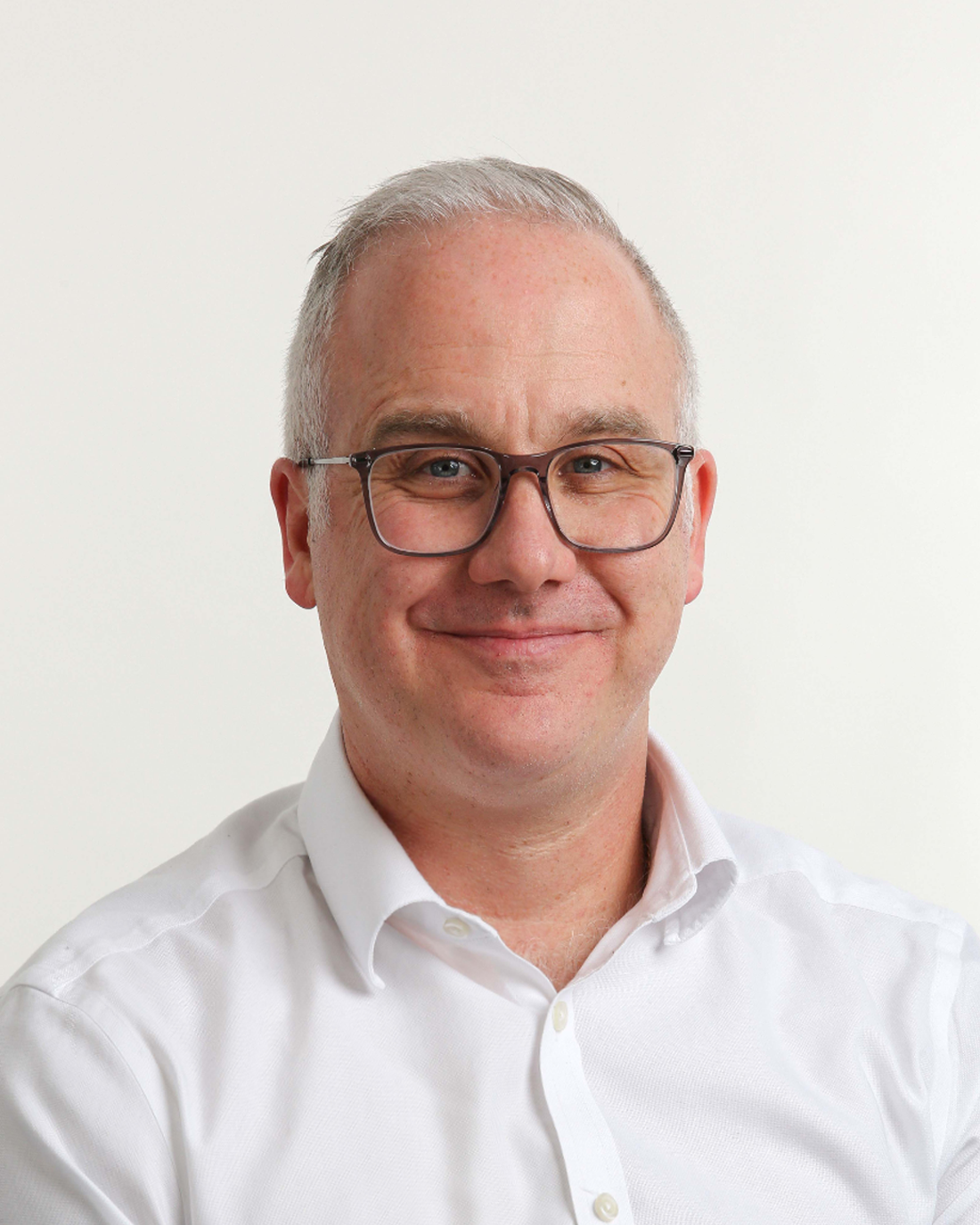 Browne Group - Smiling man with glasses and short gray hair, wearing a white shirt, in front of a plain light background.