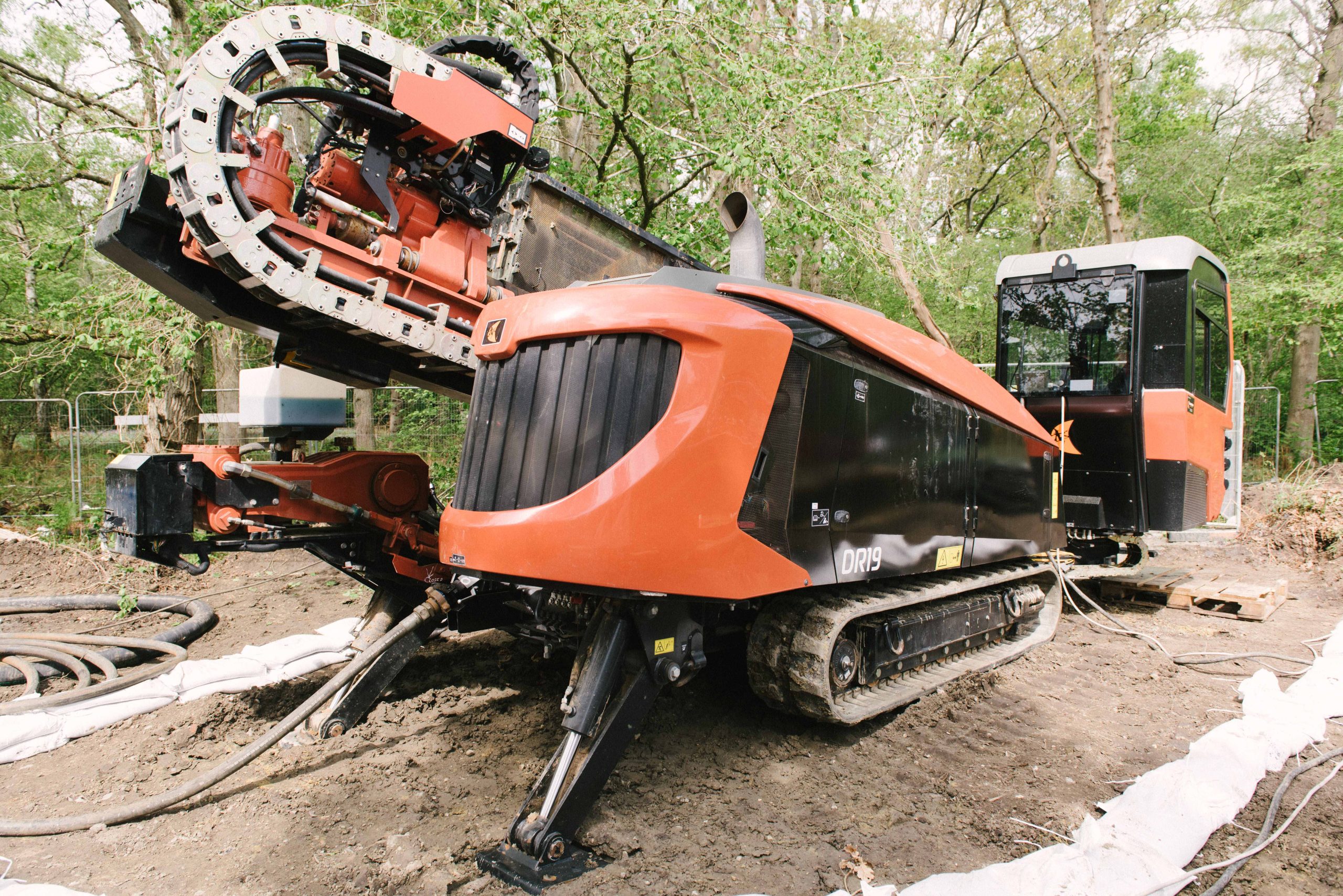 Browne Group - Large orange and black drilling machine on tracks positioned at a construction site near trees.