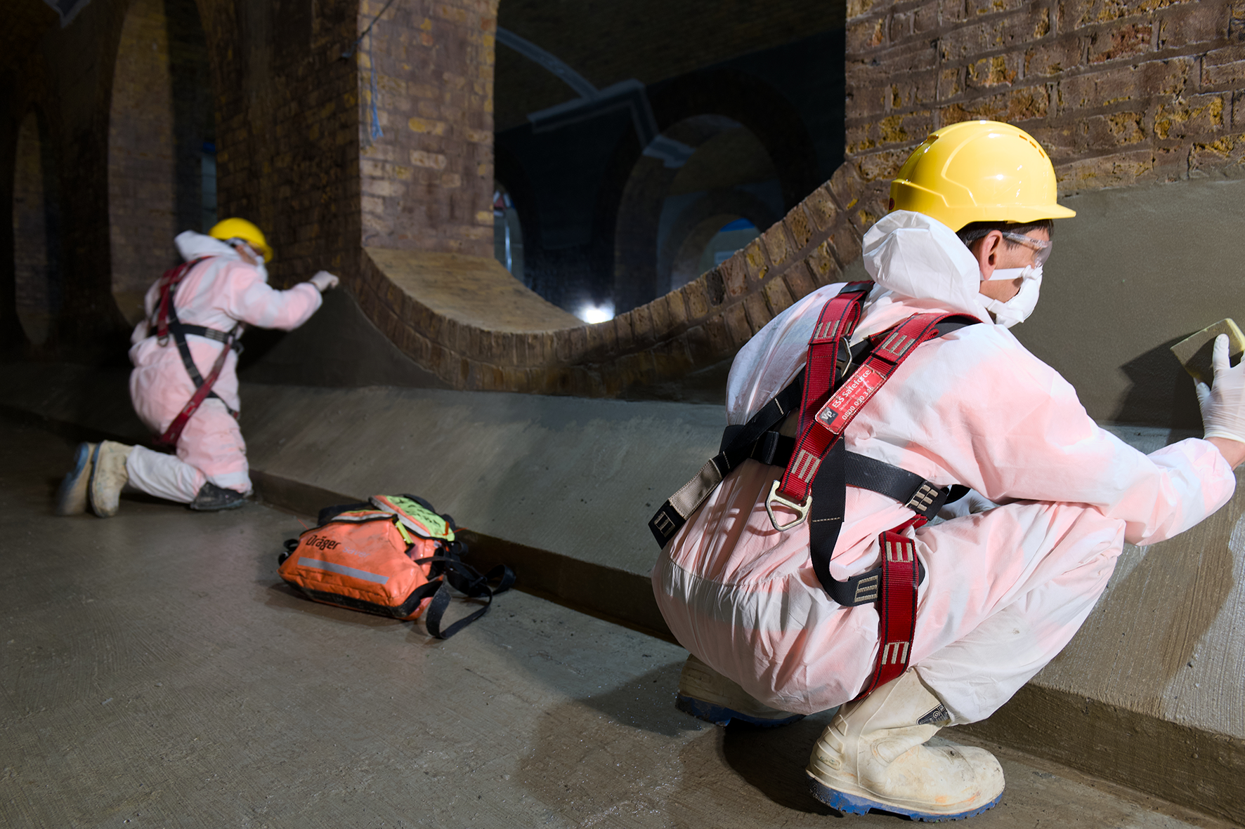 Browne Group - Two workers in protective gear and helmets apply material to a curved wall in an industrial setting.