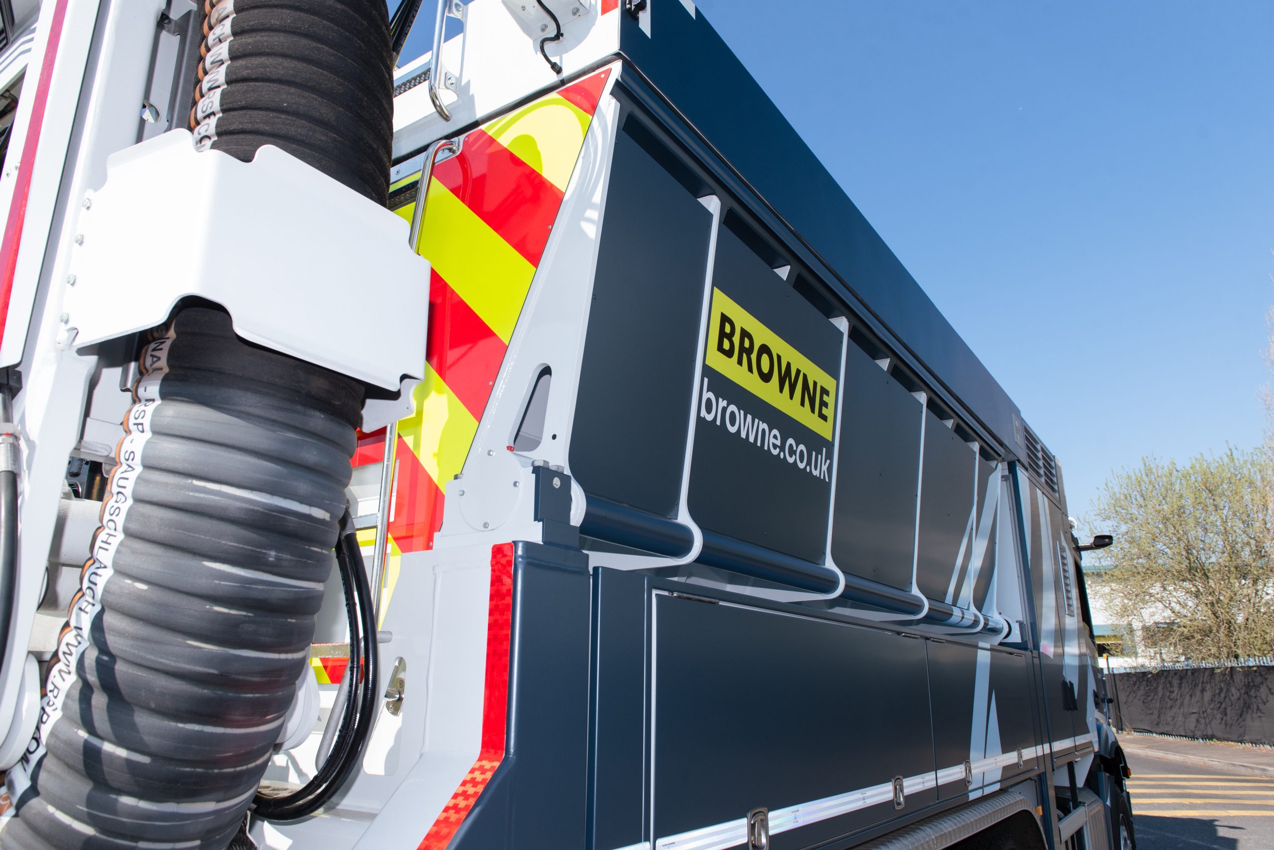 Browne Group - Side view of a blue industrial vehicle with “BROWNE” logo and safety stripes, taken on a sunny day.