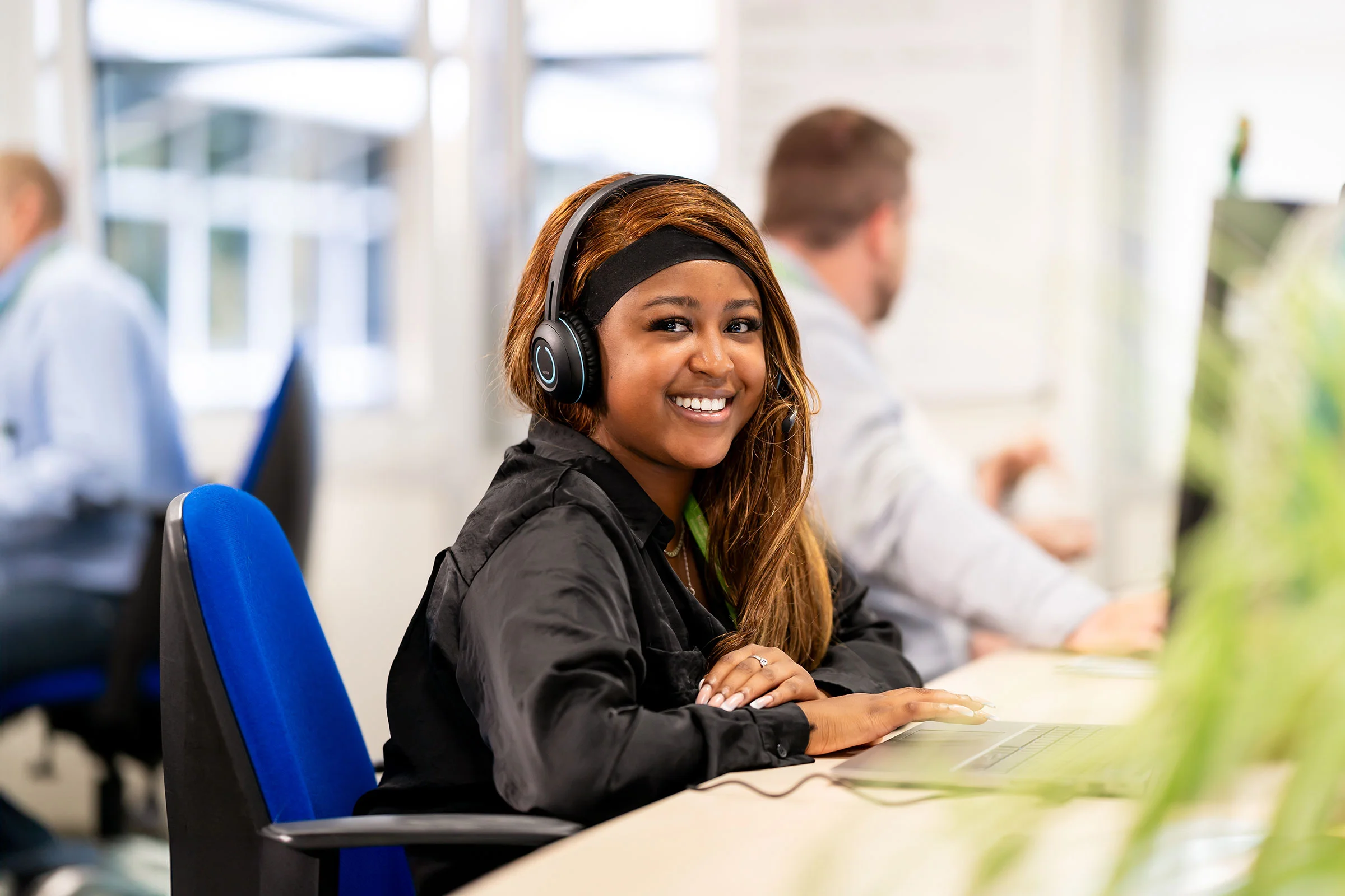 Browne Group - Woman with headset smiling at desk in an office, with colleagues working in the background.