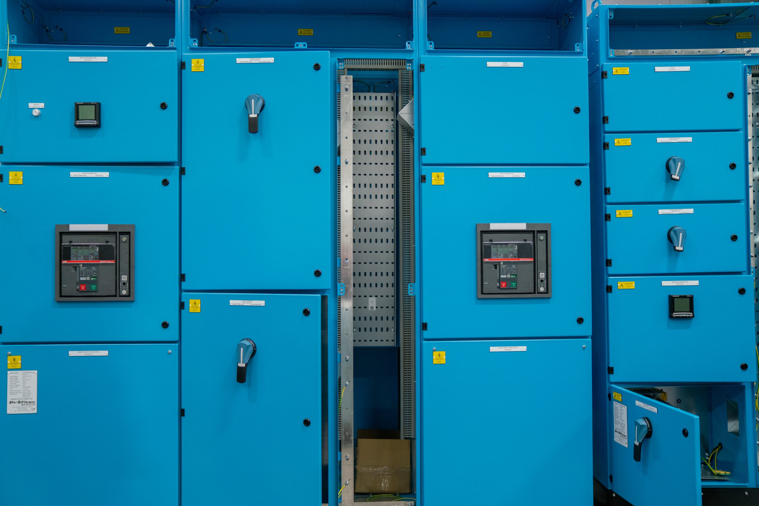 Browne Group - Rows of blue electrical control panels with switches, meters, and an open central panel exposing wiring.