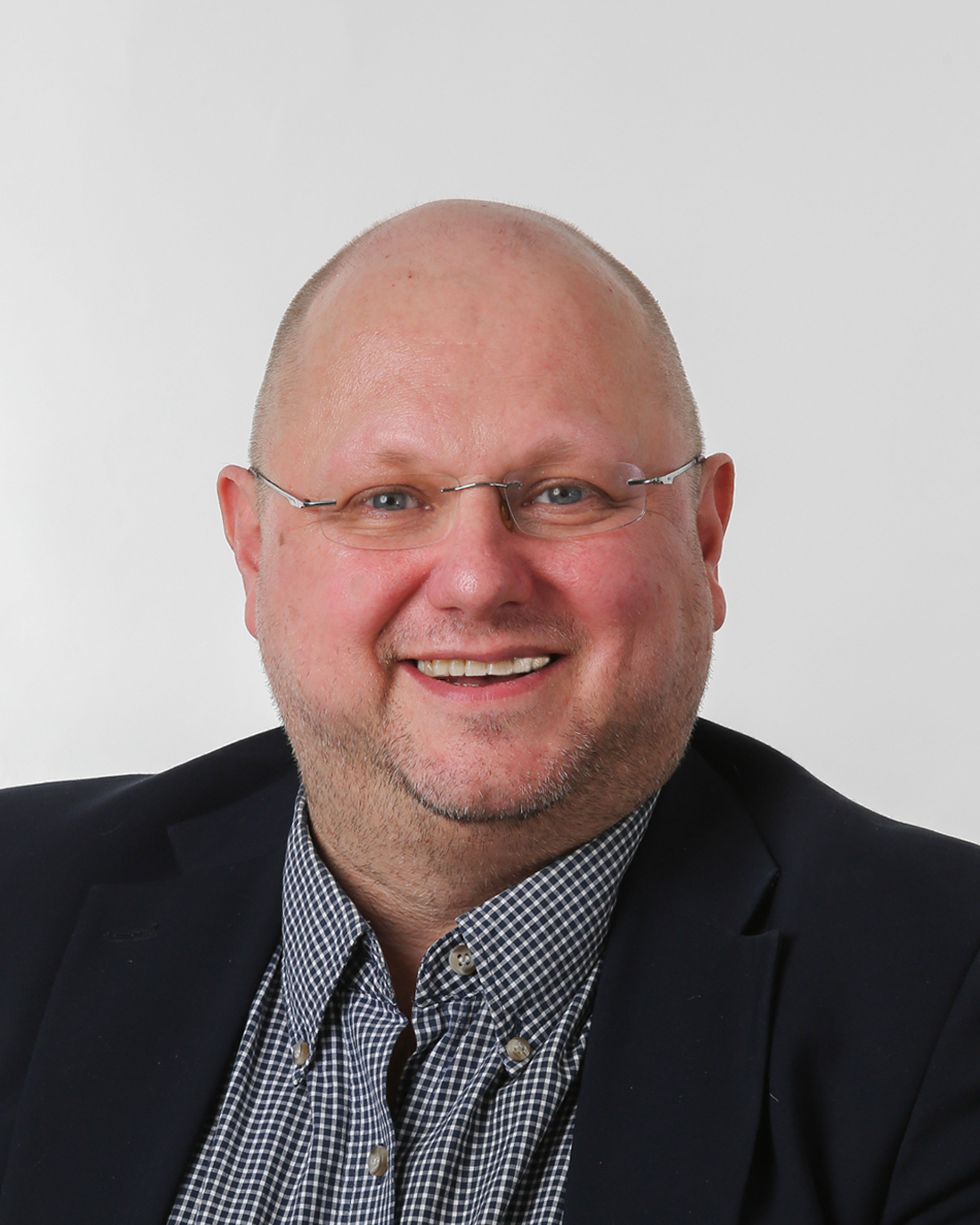 Browne Group - A smiling man with glasses, a beard, and a blazer, posing in front of a plain white background.