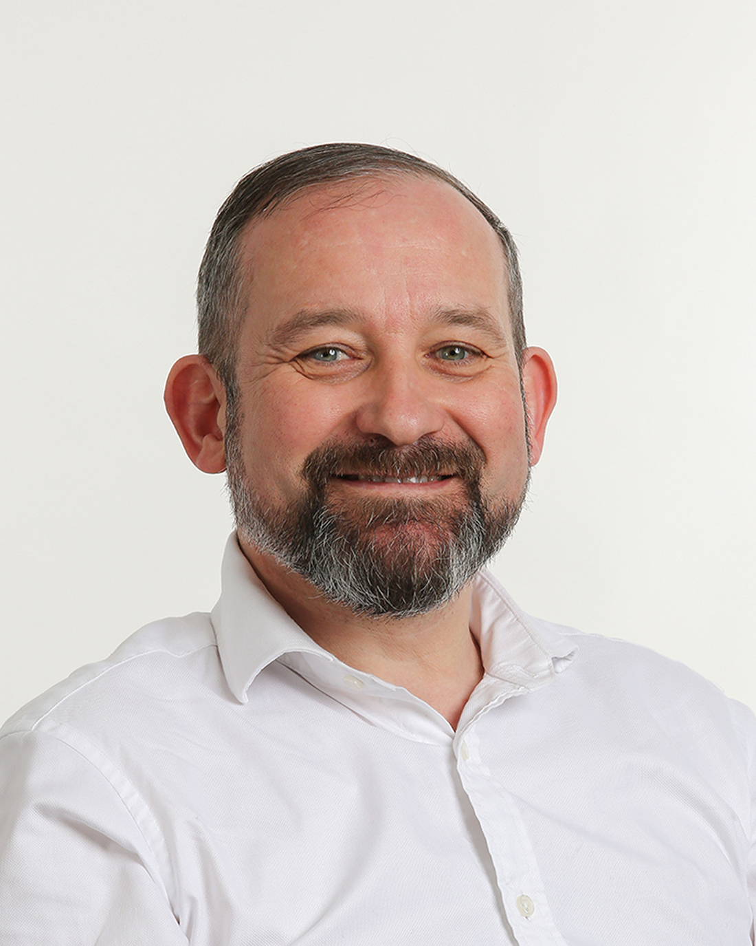 Browne Group - Smiling man with a beard and short hair, wearing a white shirt, against a plain white background.