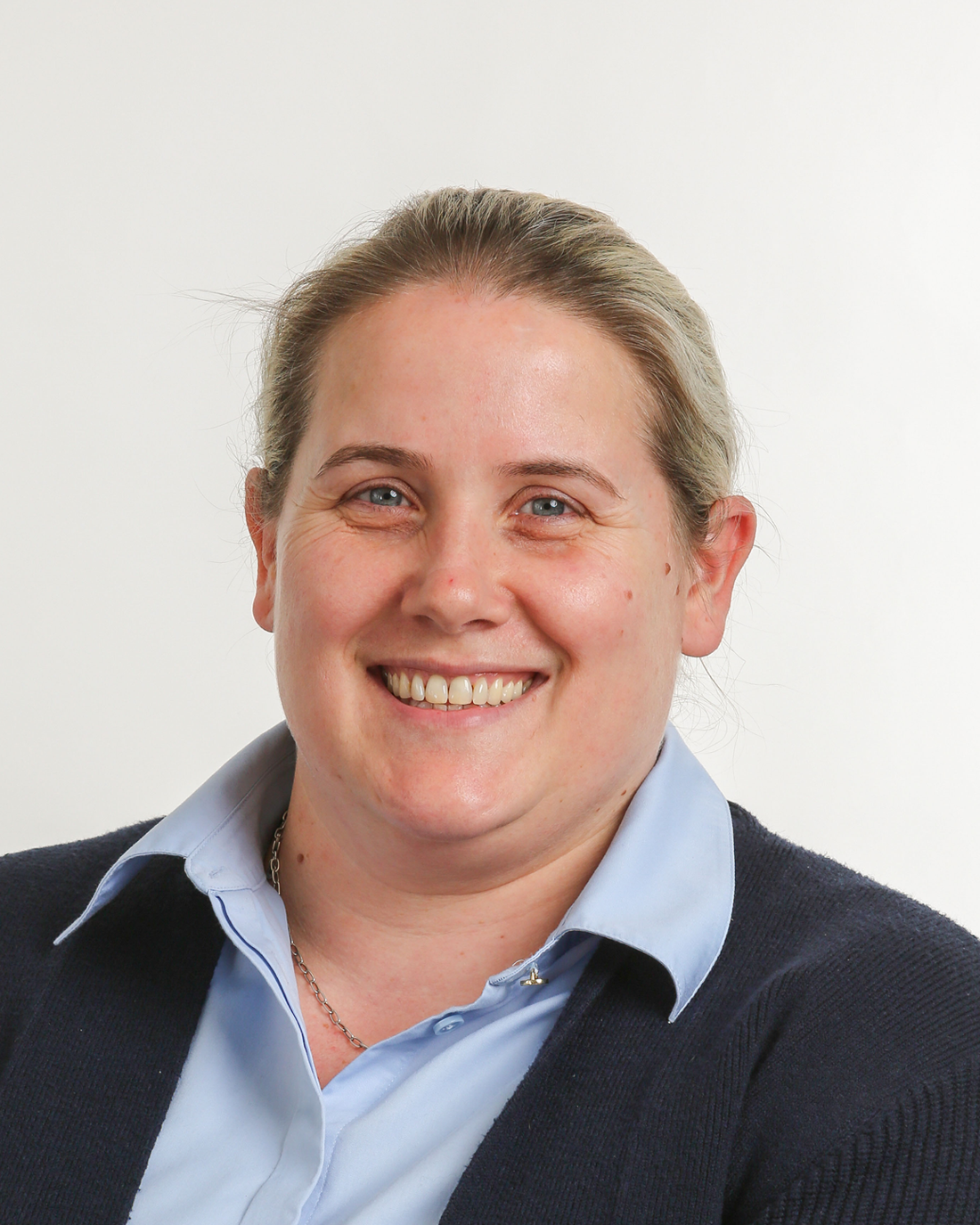 Browne Group - Smiling woman with blonde hair wearing a blue shirt and dark sweater against a plain white background.