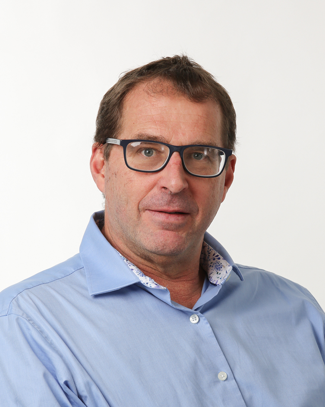 Browne Group - A man with short brown hair, glasses, and a blue shirt poses against a plain white background.