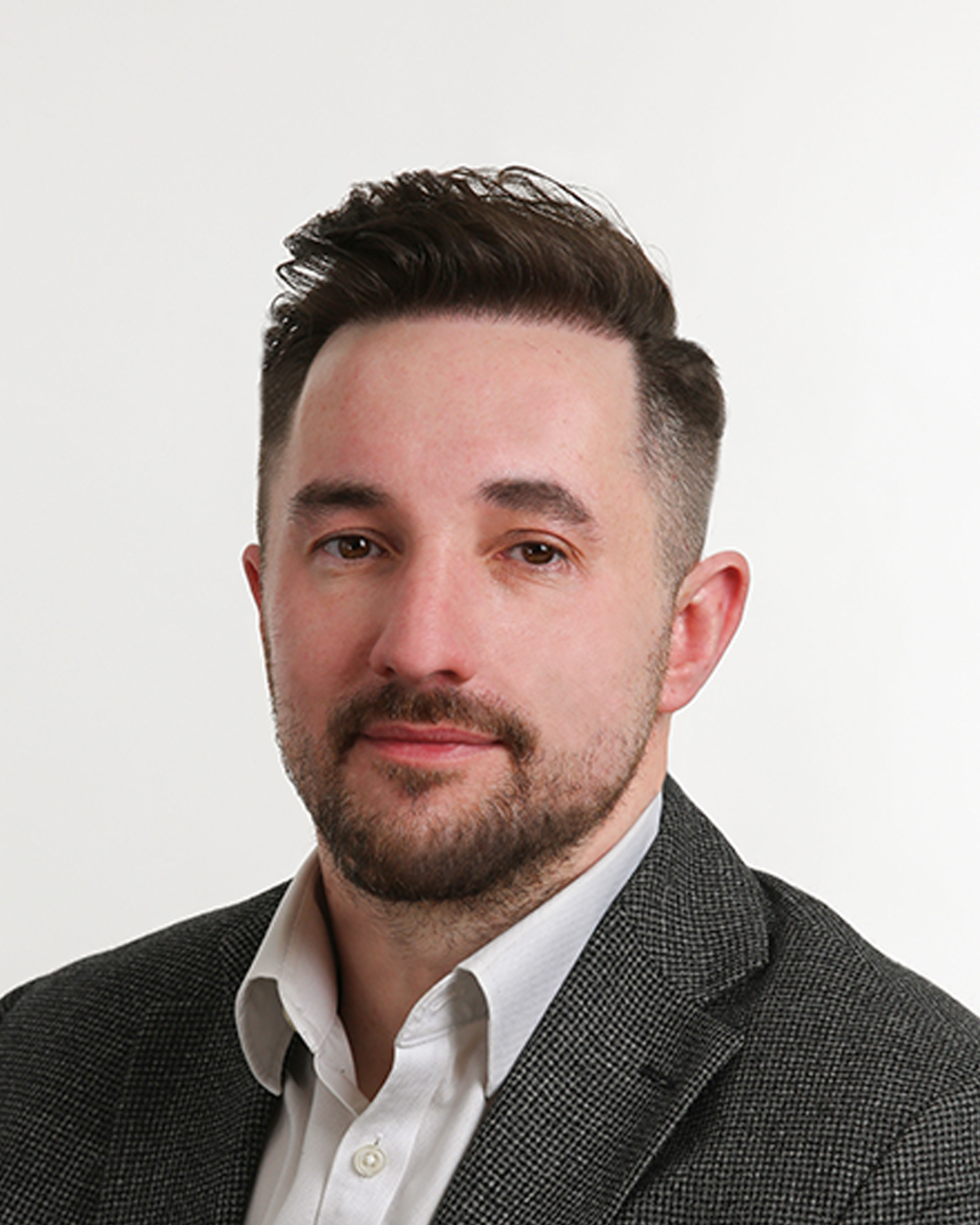 Browne Group - Man with short dark hair and beard in a grey blazer and white shirt, facing the camera, neutral background.