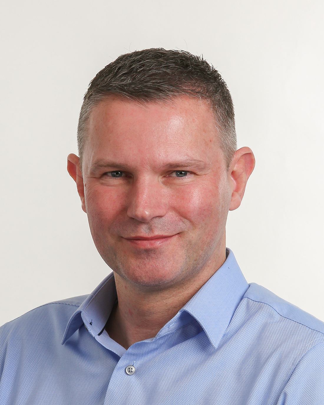 Browne Group - Smiling man with short brown hair in a light blue collared shirt against a plain white background.