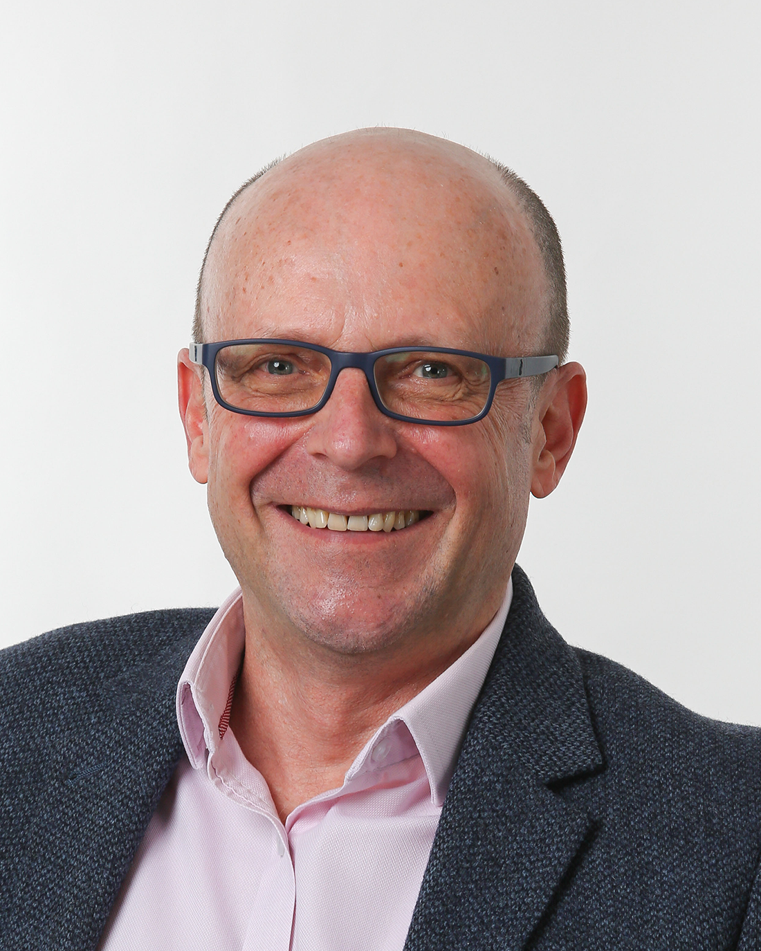 Browne Group - Smiling middle-aged man with glasses, wearing a blazer and light pink shirt, against a plain background.