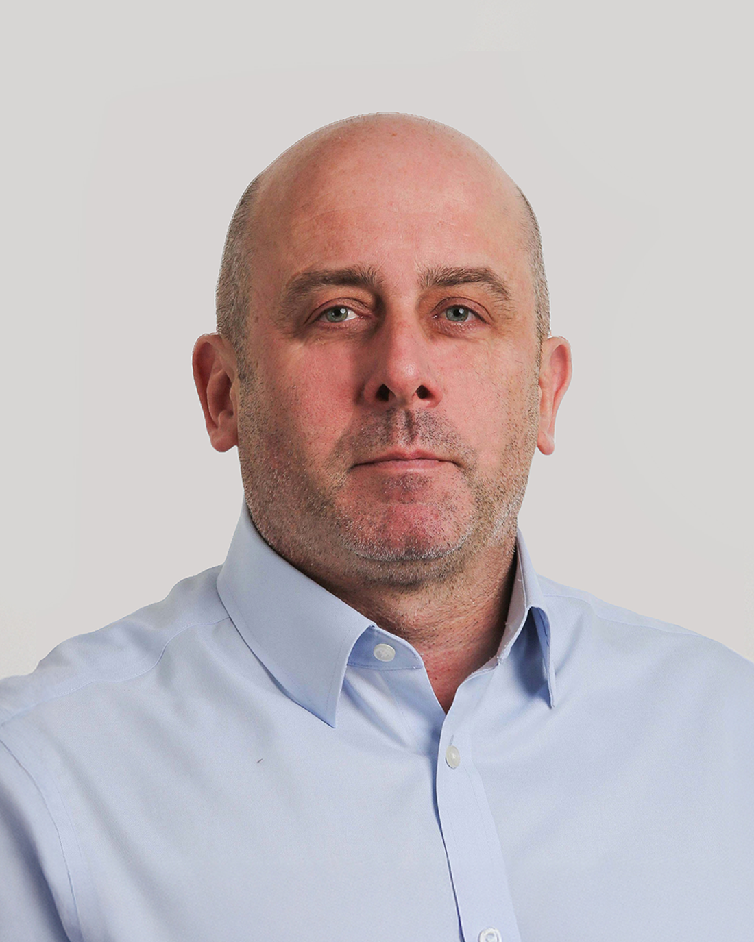 Browne Group - A man with a shaved head and stubble wearing a light blue button-up shirt, facing forward.